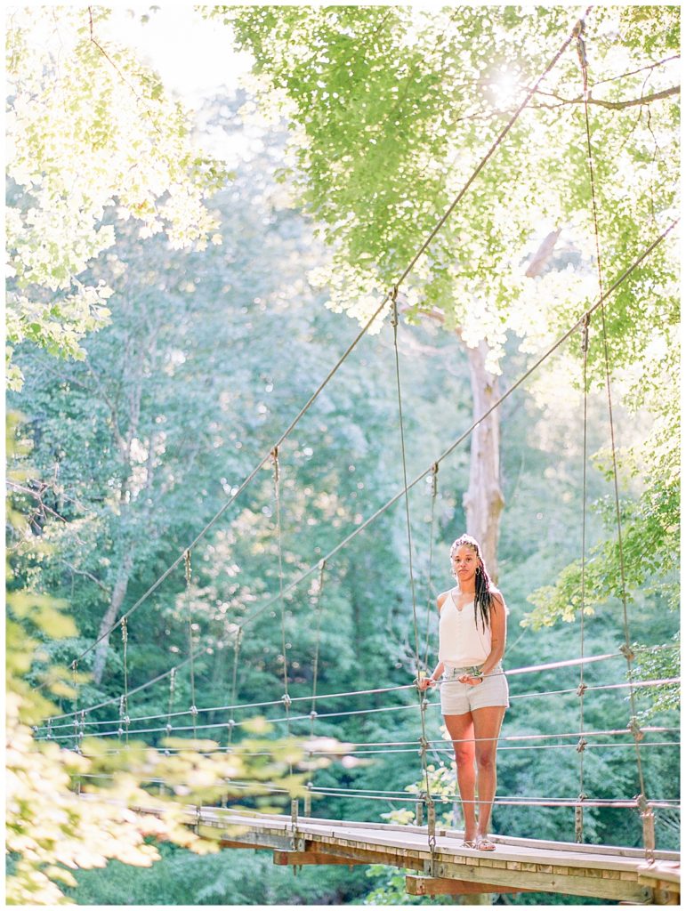 woman standing on hanging bridge at eno river state park with sunset behind her