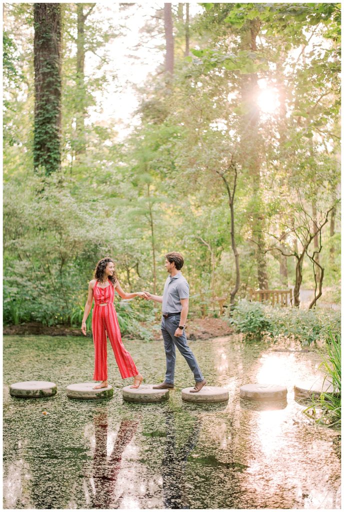 engaged couple crossing stepping stones over a pond
