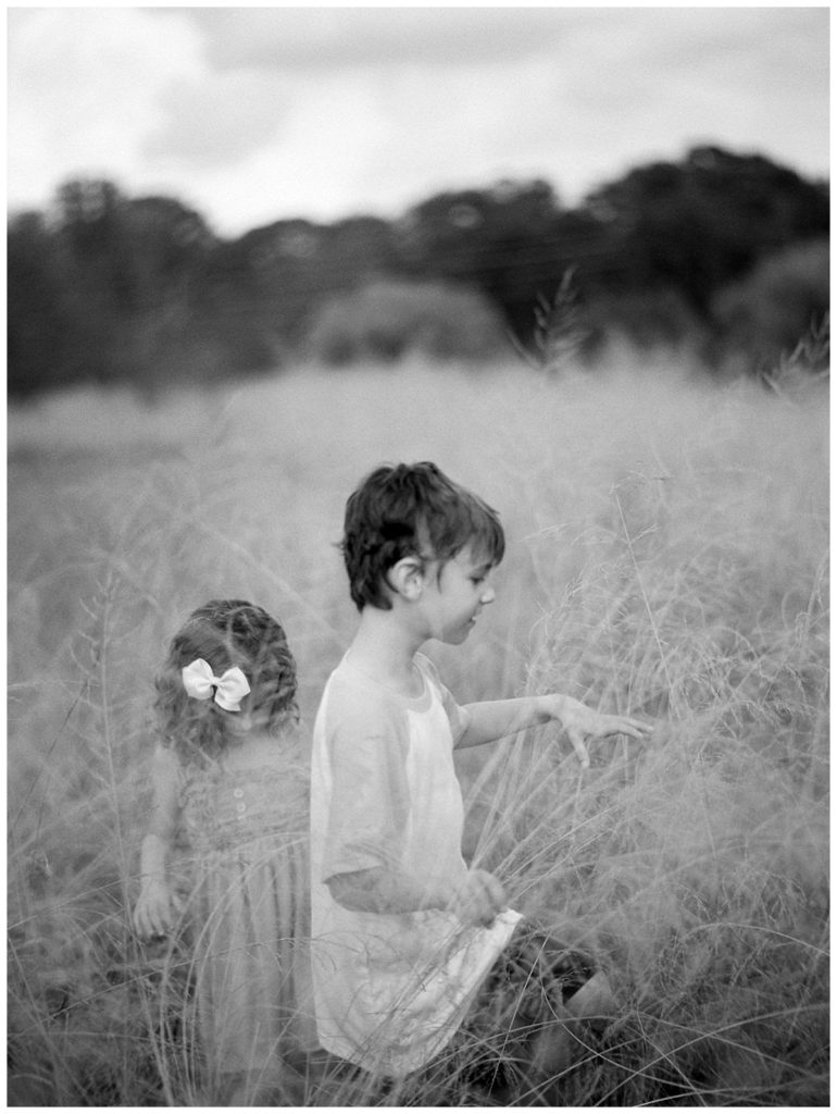 children exploring in tall grass black and white photography