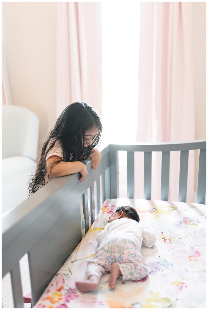 big sister looking at baby sister in crib